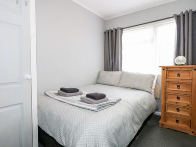 A bedroom with a bed, bedside chest of drawers, and window with curtains at 98 Cherry Park in Chapel St Leonards