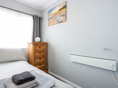 A bedroom with a bed a wooden chest of drawers and a wall heater at 98 Cherry Park in Chapel St Leonards