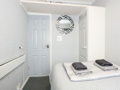 A bedroom with two closed doors a bed with folded towels and a round mirror on the wall at 98 Cherry Park in Chapel St Leonards