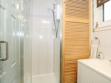 A bathroom shower area with glass door wooden cabinet and white sink at 98 Cherry Park in Chapel St Leonards