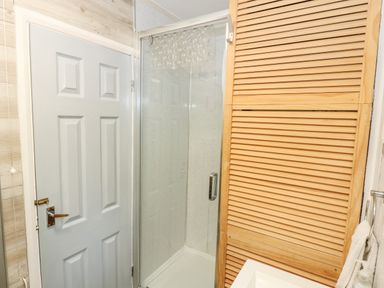 A bathroom with a white door shower with glass door and wooden louvered cabinet at 98 Cherry Park in Chapel St Leonards