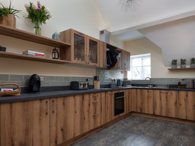 A kitchen with wooden cabinets black countertop appliances and flowers on a shelf at The Belfry in Windermere