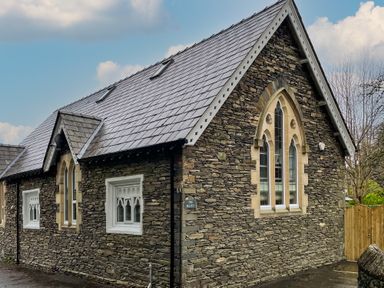 A stone building with arched windows and a gray tiled roof at The Belfry in Windermere