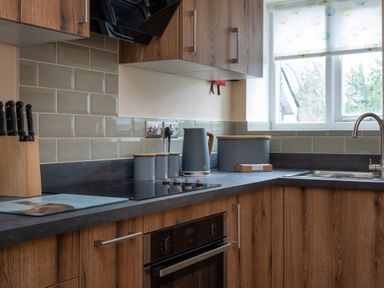 A kitchen corner with wooden cabinets a black countertop a stovetop an oven a knife block a kettle storage canisters and a window at The Belfry in Windermere