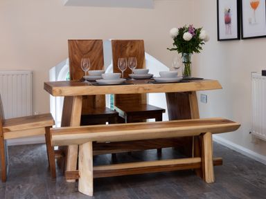 A dining area with a wooden table set with plates bowls and glasses and a wooden bench and chairs at The Belfry in Windermere