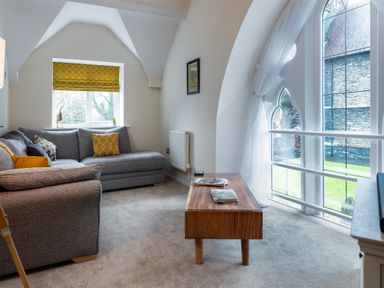 A sitting area with a grey sofa wooden coffee table and large arched windows at The Belfry in Windermere