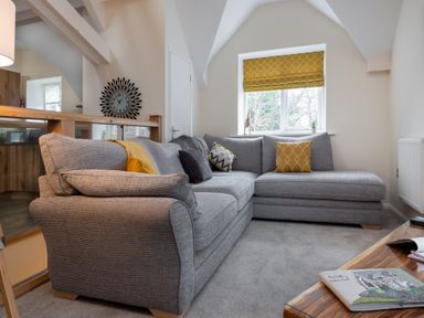 A living room with a gray sectional sofa and yellow cushions by a window with a yellow blind at The Belfry in Windermere