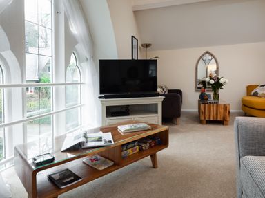 A living room with a wooden coffee table magazines a tv on a stand and a yellow armchair at The Belfry in Windermere