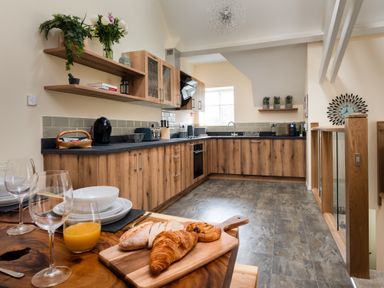 A kitchen with wooden cabinets dining table with glasses and bread at The Belfry in Windermere