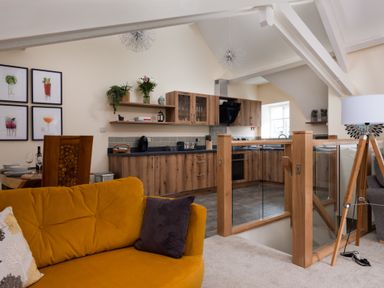 An open plan living room and kitchen with a yellow sofa wooden kitchen cabinets and a floor lamp at The Belfry in Windermere