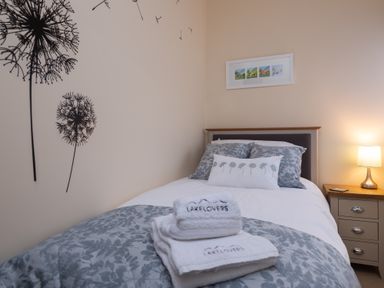A bedroom with a bed with patterned bedding towels on the bed a bedside table with a lamp and a framed picture on the wall at The Belfry in Windermere
