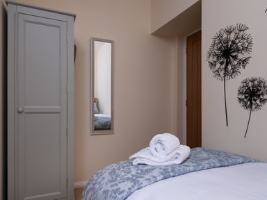 A bedroom with a bed covered by a floral blanket and white towels on top a gray wardrobe a wall mirror and dandelion wall art at The Belfry in Windermere