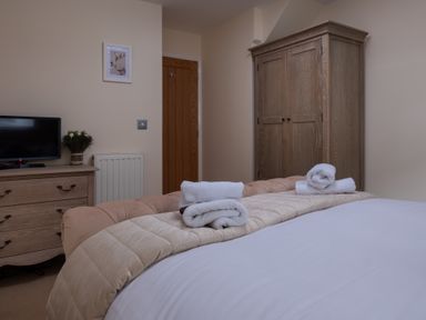 A bedroom with a bed, wardrobe, dresser with a television and flowers at The Belfry in Windermere