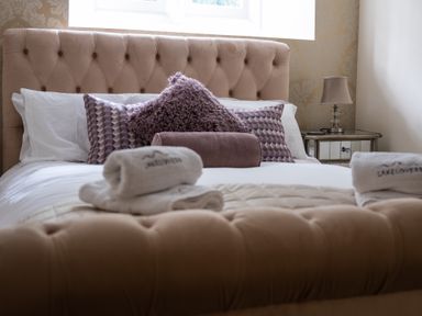 A bedroom with a tufted beige headboard pillows and folded towels on the bed at The Belfry in Windermere