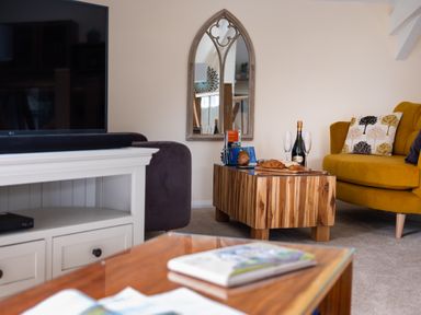 A living room with a yellow armchair a wooden coffee table with wine and snacks and a wall mirror at The Belfry in Windermere