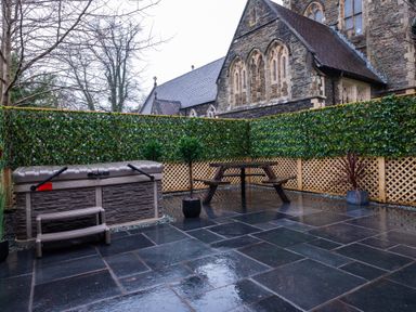 An outdoor patio area with a hot tub bench and wooden picnic table surrounded by green lattice fencing near a stone building at The Belfry in Windermere