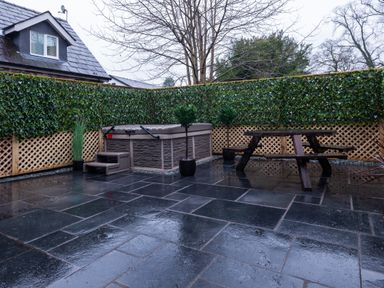 An outdoor patio area with a hot tub wooden picnic table plants and a privacy fence covered with greenery at The Belfry in Windermere