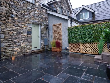 An outdoor patio area with stone and brick walls a green door plants and lattice fencing at The Belfry in Windermere