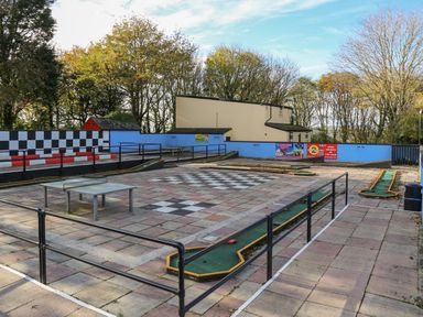 An outdoor mini golf course with a checkered area and railings surrounded by trees at Miles Retreat in Hayle