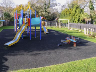 A playground with slides a swing set and a spring rocker on a rubber safety surface at Miles Retreat in Hayle