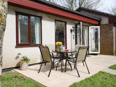 Outdoor patio with a glass table and four chairs near doors and windows of a house at Miles Retreat in Hayle