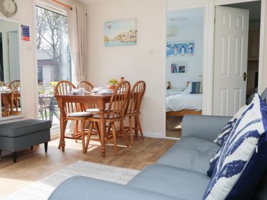 A dining area with wooden table and chairs next to a gray sofa and an open door showing a bedroom at Miles Retreat in Hayle