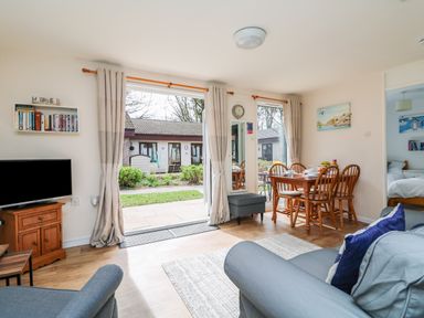 A living room with a dining table and chairs and a television on a wooden cabinet at Miles Retreat in Hayle