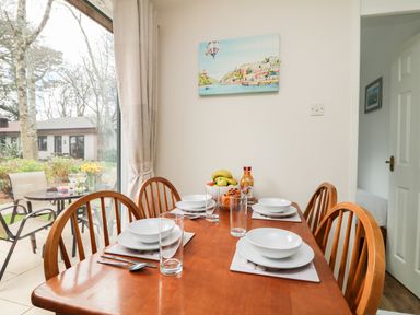 A dining table set for four with plates bowls glasses and cutlery next to a window showing an outdoor patio with chairs and a table at Miles Retreat in Hayle
