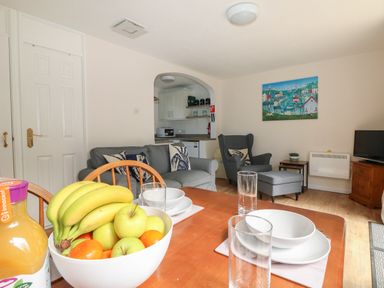 A dining table with fruit bowl and glasses in a living room with sofa armchair and kitchen at Miles Retreat in Hayle