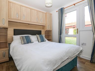 A bedroom with a double bed and wooden overhead cabinets next to a door with striped curtains at Miles Retreat in Hayle