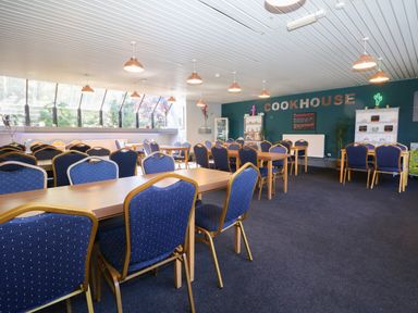 A dining area with multiple tables and blue padded chairs under hanging lights at Miles Retreat in Hayle