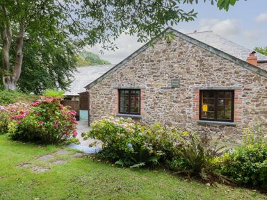 A stone cottage with two windows and flower bushes in front at The Roundhouse in Warbstow
