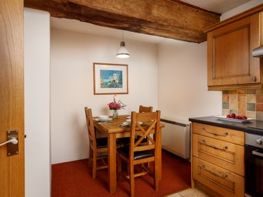 A dining area with a wooden table and four chairs set with plates and cutlery a kitchen counter with drawers and tiled backsplash and a framed picture on the wall at The Roundhouse Warbstow