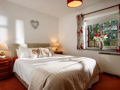 A bedroom with a large bed two bedside tables with lamps a window with curtains and a vase of flowers at The Roundhouse in Warbstow