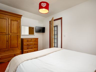 A bedroom with wooden wardrobe and chest of drawers a wall-mounted tv and an open door at The Roundhouse in Warbstow