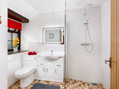 A bathroom with a toilet sink mirror glass shower partition and a window with red blind at The Roundhouse in Warbstow