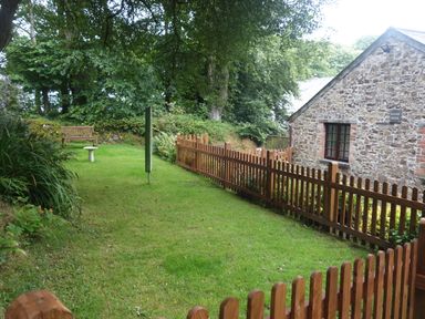 A garden with a wooden bench a small table and a picket fence next to a stone house at The Roundhouse in Warbstow