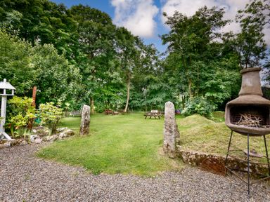 A garden with a stone pathway chiminea picnic tables and benches surrounded by trees at The Roundhouse Warbstow