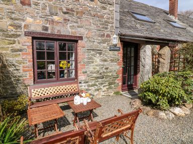 Outside seating area with wooden benches and a table in front of stone wall cottage at Ash Cottage in Warbstow