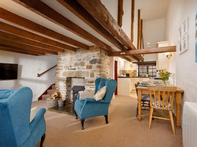 A living room with blue armchairs a stone fireplace a wooden dining table and a kitchen area at Ash Cottage Warbstow