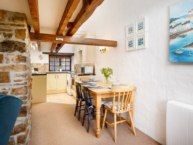 A kitchen and dining area with a wooden dining table and chairs under exposed wooden beams at Ash Cottage in Warbstow