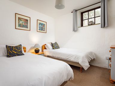 A bedroom with two single beds bedside table with lamp two framed pictures on wall and a window with curtains at Ash Cottage in Warbstow