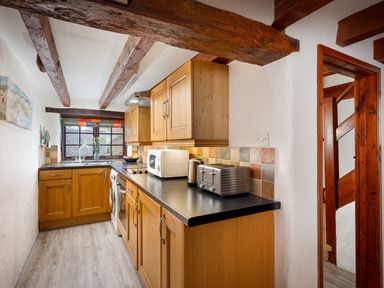 A kitchen with wooden cabinets countertop appliances and a window with a colorful valance at Pond Meadow in Warbstow