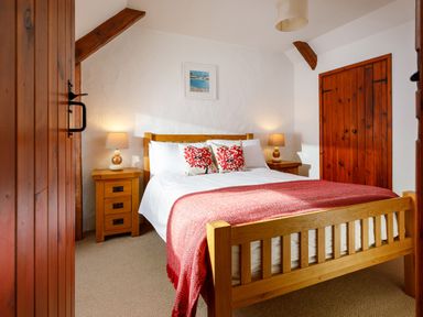 A bedroom with a wooden bed with white bedding and red cushions and throw at Pond Meadow in Warbstow