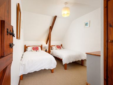 A bedroom with two single beds a wooden door a wooden beam and a chest of drawers at Pond Meadow in Warbstow