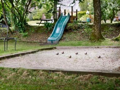 An outdoor area with a bocce ball court several balls a green slide a metal chair and trees at Pond Meadow in Warbstow