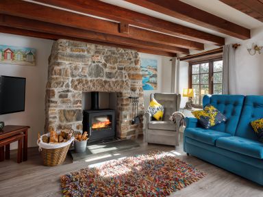A living room with a stone fireplace wood stove armchair blue sofa and colorful rug at Pond Meadow in Warbstow