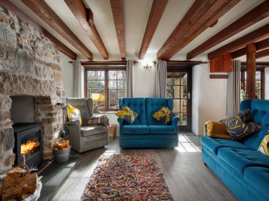 A living room with stone fireplace wood stove blue sofas armchair and multicolored rug at Pond Meadow in Warbstow