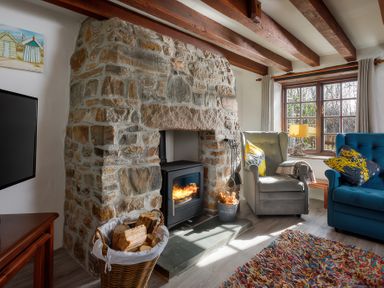 A living room with a stone fireplace wood stove two armchairs and a window at Pond Meadow in Warbstow