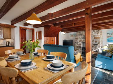 A dining area with a wooden table set for six beside a living room with blue sofas and a stone fireplace at Pond Meadow in Warbstow